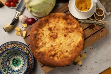 Geleneksel desenli dekoratif ulusal Özbek seramik tabaklarının yanında lahana, ot ve peynirli sıcak Osetya turtası. Çay için klasik oryantal hamur işleri.