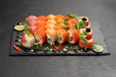 Siyah dikdörtgen taş levhada farklı suşi maki çeşitlerinden oluşan büyük bir set. Haşlanmış pirinç ve Norveç yosununa sarılı geleneksel bir çiğ balık ve deniz ürünleri tabağı..