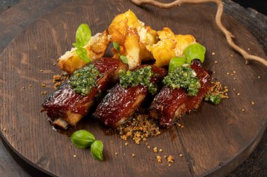 Izgara kuzu kaburgası, yanında patates, fesleğen ve ahşap kesim tahtasında aioli sosu..