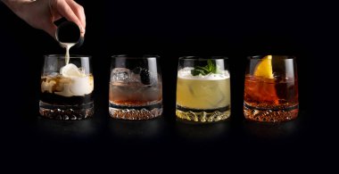 Girl bartender pours cream and prepares a set of classic cold alcoholic cocktails in transparent glasses on a black background. White Russian, Bramble, Whiskey Sour and Negroni. clipart