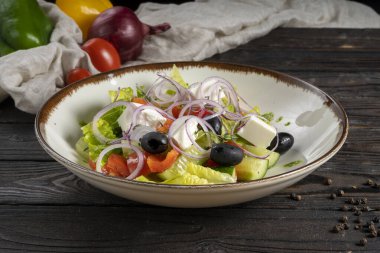 Peynirli sebze salatası. Marul, zeytin, kırmızı çan biberi, kiraz domatesleri, soğan halkaları, salatalık ve peynir küpleri ahşap mutfak masasında seramik tabakta. Soğuk meze..