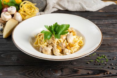 Tavuk ve mantarlı Tagliatelle. Makarna, tavuk fileto, mantar, peynir, Fransız hardalı, sos ve maydanozu seramik tabakta ahşap mutfak masasında..