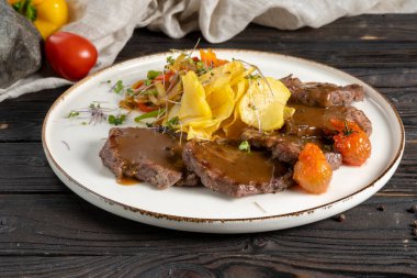 Et soslu biftek, kızarmış patates ve sebze. Tahta mutfak masasında seramik tabakta sebzeli dana eti ya da helal et yemeği..