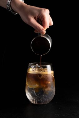 Kız barmen kokteyl hazırlar ve espresso toniğine kahve koyar. Soğuk alkollü kahve kokteyli ve siyah arka planda şeffaf bardakta ferahlatıcı bir tonik..