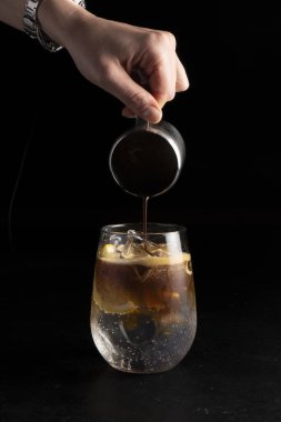 Girl bartender prepares a cocktail and pours coffee into an espresso tonic. Cold alcoholic cocktail of coffee and a refreshing tonic in a transparent glass on a black background. clipart