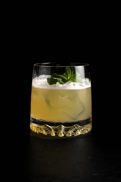 Whiskey sour cocktail. Cold alcoholic cocktail of quail egg protein, lemon juice, sugar syrup, bourbon, bitter, mint and ice in a transparent glass on a black background.