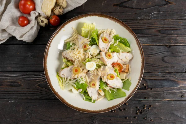 Caesar salad with chicken fillet. Lettuce, olives, cheese, cherry tomatoes, quail egg, and crunchy croutons in a ceramic plate on a wooden kitchen table. Cold appetizer. — Stock Image Caesar Salad Chicken Fillet Lettuce Olives Cheese Cherry Tomatoes Quail Stock Image