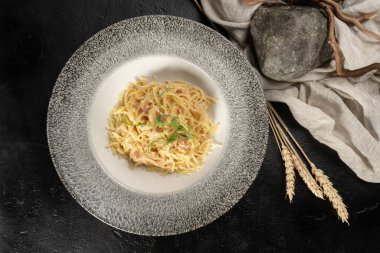 Peynirli ve pastırmalı spagetti. Durum buğdaylı makarna. Siyah taş bir masada sıcak bir ana yemek. Bir tabak makarnanın yanında mısır gevreği..