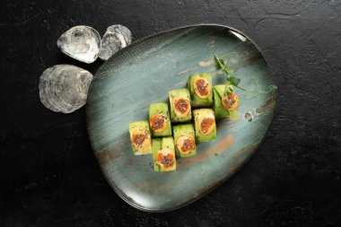Avokadoya sarılmış suşi ruloları. Seramik tabakta bir porsiyon suşi..