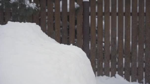Un uomo con una pala da neve getta la neve su un grande cumulo di neve — Video Stock