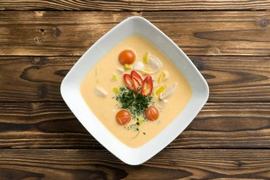 Geleneksel Tayland baharatlı hindistan cevizi çorbası tavuk göğsü ve ahşap mutfak masasında beyaz kare şeklinde seramik tabakta kırmızı biber. Asya mutfağının ilk yemeği. Üst görünüm