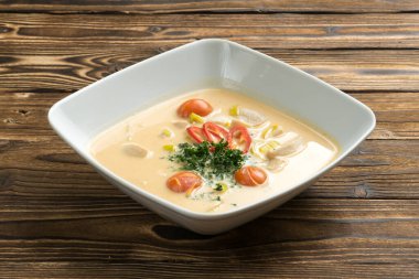 Geleneksel Tayland baharatlı hindistan cevizi çorbası tavuk göğsü ve ahşap mutfak masasında beyaz kare şeklinde seramik tabakta kırmızı biber. Asya mutfağının ilk yemeği..