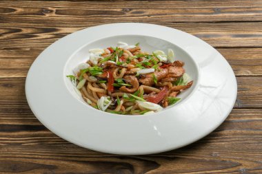 Tavuklu Çin eriştesi dolmalık biber ve teriyaki soslu soğan. Beyaz seramik tabakta ahşap mutfak masasında sıcak Asya makarnası ve kümes hayvanı eti..