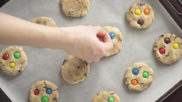 A woman decorates a raw cookie on a baking sheet with colorful M&Ms candies — Stock Video