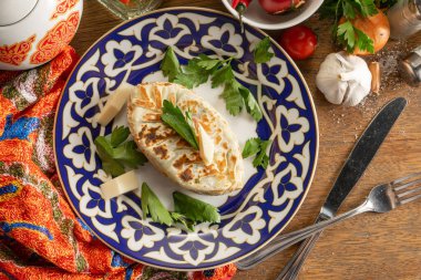 Otlu ve peynirli Kok-samsa. Suluguni peyniri ve geleneksel Özbek desenli bir tabakta bitkilerle ince hamurdan yapılmış düz ekmek.