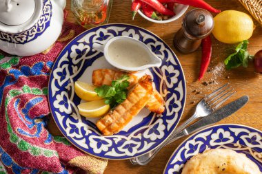 Ulusal Özbek desenli bir tabakta limonlu, peynirli ve maydanozlu ızgara somon filetosu.