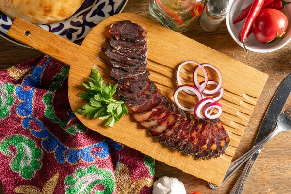 Slices of homemade dried horse meat sausage with coriander and red onion, sliced and served on a wooden chopping board