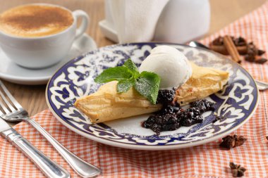 Meyve reçelli puf böreği ve geleneksel Özbek desenli bir tabakta nane yaprağıyla süslenmiş vanilyalı dondurma topu.