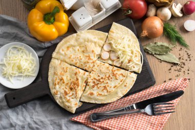 Tahta kesme tahtasının üzerinde sosisli ve mozzarella peynirli düz ekmek.