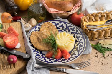 Geleneksel Özbek desenli bir tabakta patates püresi, sebze ve dereotlu balık pirzolası