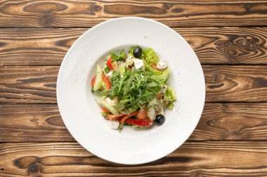 Beyaz seramik tabakta roka, zeytin ve peynir ile vejetaryen Yunan sebze salatası.