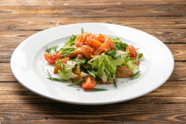 Beyaz seramik tabakta somon, patates ve kiraz domatesli vejetaryen sebze salatası.