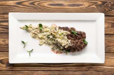 Mantarlı biftek ve beyaz seramik tabakta kereviz sosu.