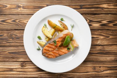 Fırında patates ve beyaz seramik tabakta limonlu ızgara somon bifteği.