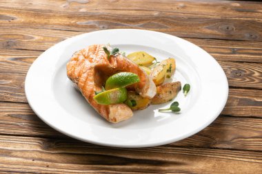 Fırında patates ve beyaz seramik tabakta limonlu ızgara somon bifteği.