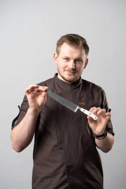 Ceketli genç bir aşçı, göğsüne yazı işlenmiş bir şef, profesyonel bir aşçının bıçağını gösteriyor ve beyaz arka planda bir portre için poz veriyor.
