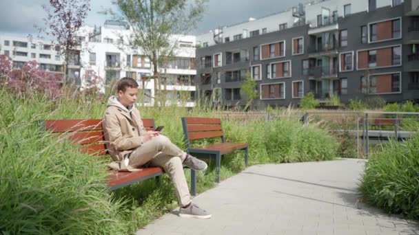 Un gars triste envoie des textos au téléphone, assis sur un banc près de la maison — Video