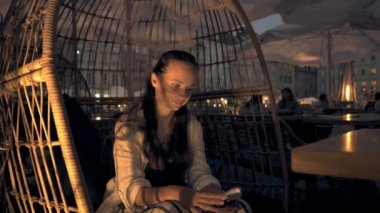 Genç ve güzel bir kadın akşamleyin oturuyor ve Warsaw Meydanı 'ndaki bir kafede hasır bir sandalyede telefona bakarak sipariş bekliyor.