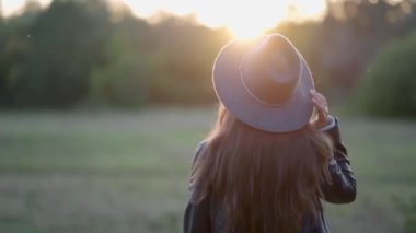 Giderken, kız arkasını döner ve gün batımında şapkasını düzeltir.