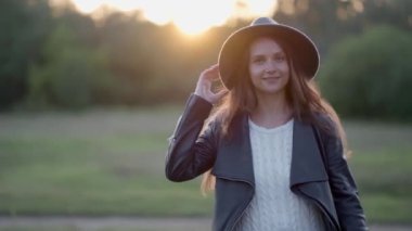 Giderken, kız arkasını döner ve gün batımında şapkasını düzeltir.