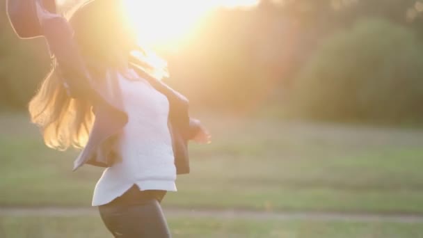 Una ragazza con un cappello, che corre gioiosamente e gira nei raggi del sole al tramonto — Video Stock