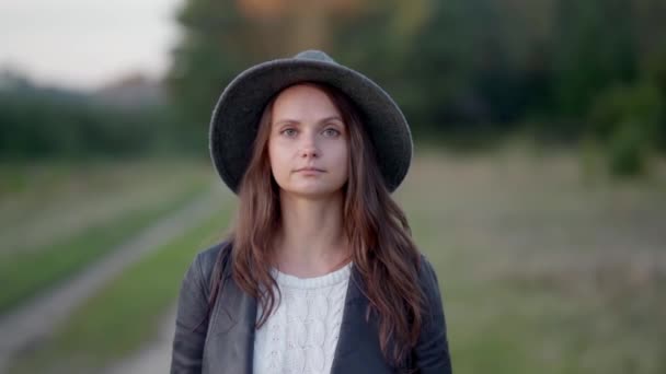 En ung kvinna i hatt går ensam i parken och tittar sorgligt på kameran. — Stockvideo