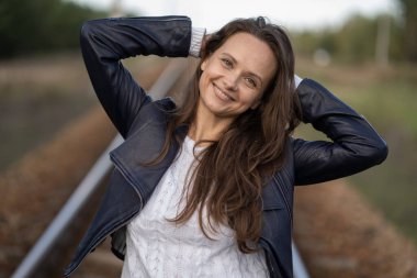 Genç ve güzel bir kız demiryolu raylarında poz veriyor ve açık bir yaz gününde kameraya bakarak gülümsüyor.