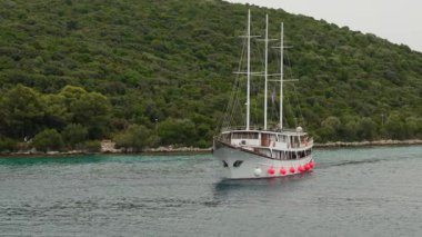 A traditional wooden gulet, a charter boat for tourist excursions, cruises in a calm bay on a cloudy day. This peaceful scene shows a scenic journey along the green Adriatic coast of Croatia.