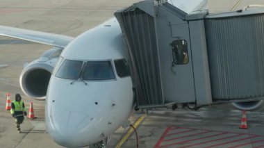 Yolcu köprüsü uçak gövdesine yanaşıyor. Bagaj yükleyicisi havaalanı apronuna yaklaşırken operatör uçağın jet yolu bağlantısını kontrol eder.