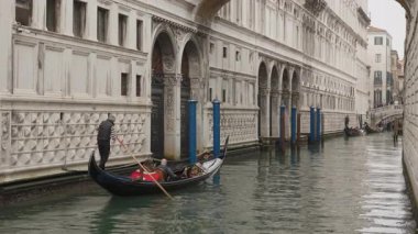 Geleneksel siyah gondollu turistler ve gondolcular Venedik İtalya 'daki tarihi bir sarayın önünde dar bir kanal boyunca kürek çekiyorlar. Otantik seyahat ve kültür turizmi.