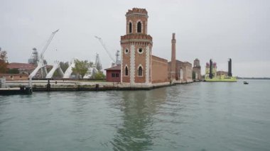 Venedik İtalya 'daki dev beyaz el heykelleri ve tarihi Arsenale kuleleri. Tuğla mimarisi, endüstriyel vinçler ve bulutlu bir günde deniz gemileriyle manzaralı bir göl manzarası..