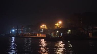 Venedik 'teki sanayi limanının gece görüşü. Rıhtımda vaporetto teknesinin inşaat vinçleri ve sokak ışıkları var. İtalya 'da karanlık su yansımaları ve kentsel akşam atmosferi.