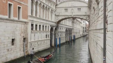 Gondolcu ve yolcular İç Çekiş Köprüsü 'nün altında dar bir kanalda kürek çekiyorlar. Venedik İtalya 'da bulutlu bir günde Doge Sarayı' nın tarihi mimarisi ve cezaevi.