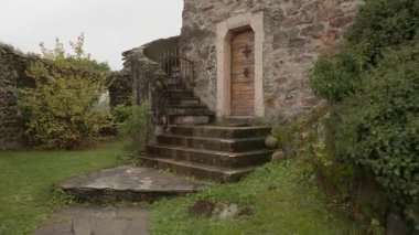 İtalya 'da ahşap kapı ve taş merdivenleri olan antik bir taş binaya giriş. Kırsal bir köy avlusundaki tarihi mimariyi çevreleyen bahçe yolu ve yeşil çalılar.