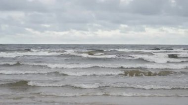 Jurmala Letonya 'da Baltık Denizi' nin kumlu sahillerinde dalgalar dalgalanır. Soğuk sonbahar okyanus suyunun üzerindeki bulutlu gökyüzü. Seyahat, çevre ve rahatlama temaları için doğa kıyı manzarası.