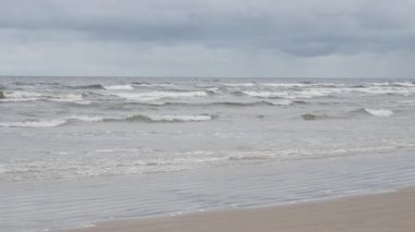 Jurmala Letonya 'da Baltık Denizi' nin kumlu sahillerinde dalgalar dalgalanır. Kumsalda, bulutlu gökyüzünün altında kum dalgaları. Doğa, seyahat ve çevre temaları için kuzey kıyı manzaraları.