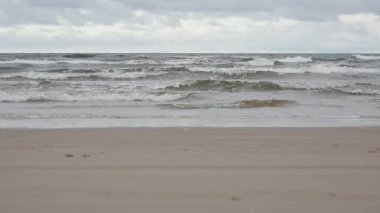 Jurmala Letonya 'daki Baltık Denizi' nin kumlu sahillerinde dalgalar akıyor. Seyahat ve çevre temaları için bulutlu gökyüzü altında kıyı manzarası alçak açılı zemin görünümü.