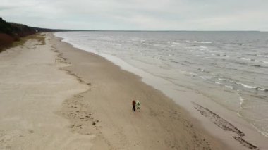 Jurmala 'da kumsalda yürüyen iki yaşlı kadın arkadaş. Dalgalı Baltık Denizi ile sonbahar manzarası ve Letonya 'da sezon dışında deniz kenarı tatil beldesinde bulutlu gökyüzü.