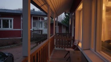 Alacakaranlıktaki kırmızı ahşap evin penceresinden gelen sıcak ışık parlıyor. Kuzey Avrupa 'da sakin bir akşamda Finlandiya' nın yerleşim bölgesine bakan verandadan manzaraya bakın..