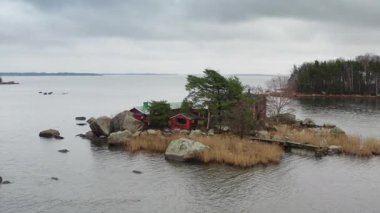 Finlandiya 'da kayalık bir adada gözlerden uzak kırmızı ahşap bir ev. Çam ağacı, sazlıklar ve kayalarla çevrili Kuzey kıyıları kasvetli bir günde sakin deniz suyuyla çevrili..